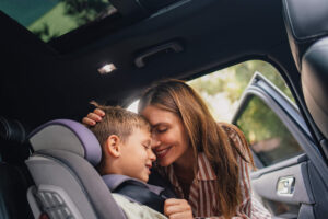 A mom hugs her little boy as she secures him in a forward-facing car seat.